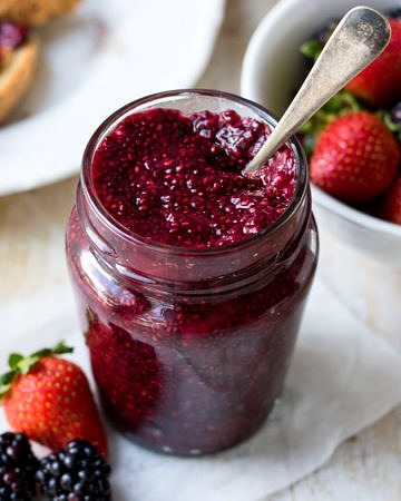 Easy mixed berry chia jam in small curved jar, spoon in the jar, berries in background