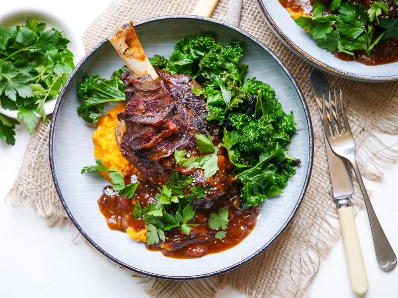 Balsamic slow cooker lamb shank on top of sweet potato mash with kale, blue bowl