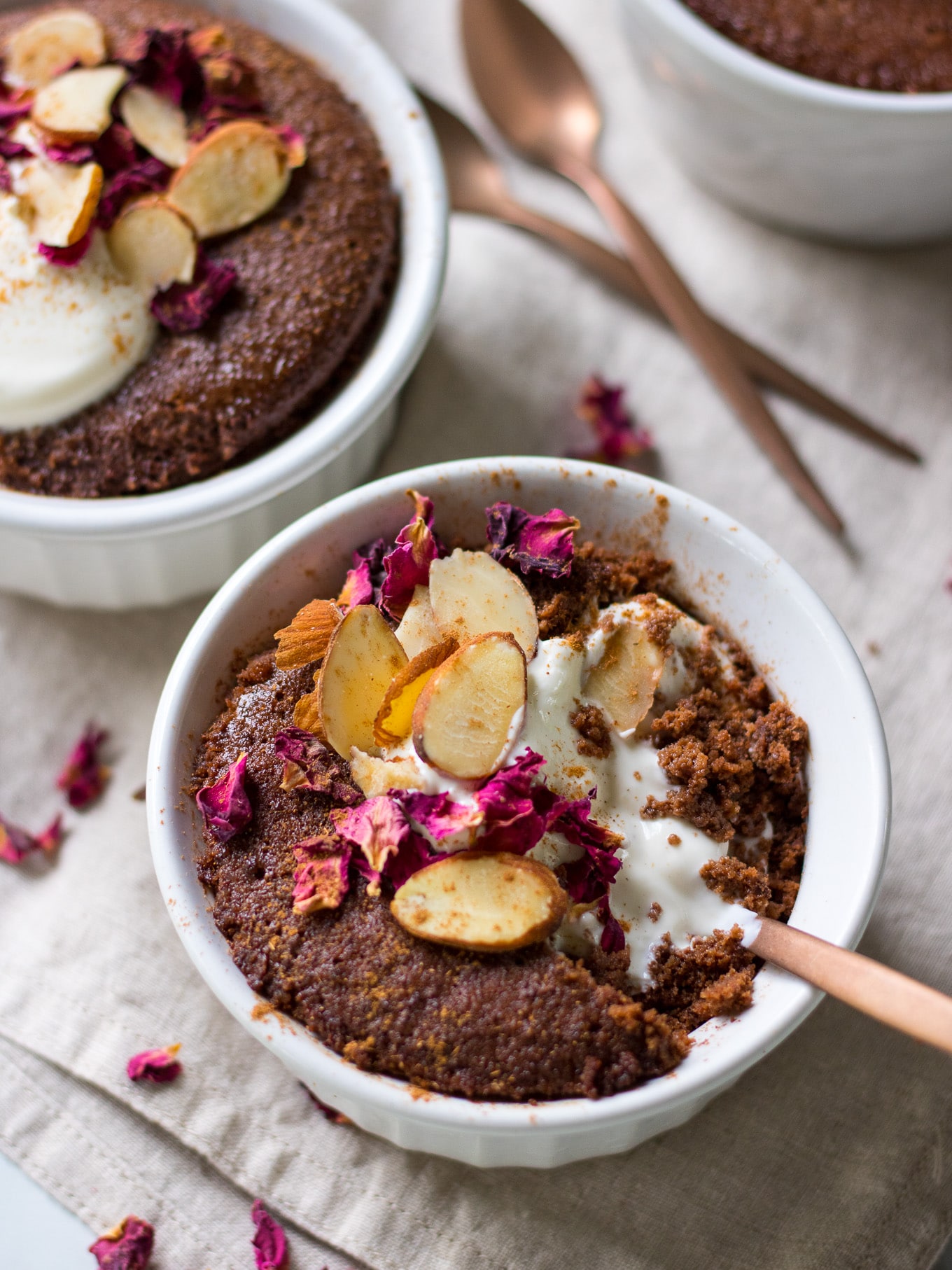 Chocolate cake in a small white ramekin topped with pink rose petals