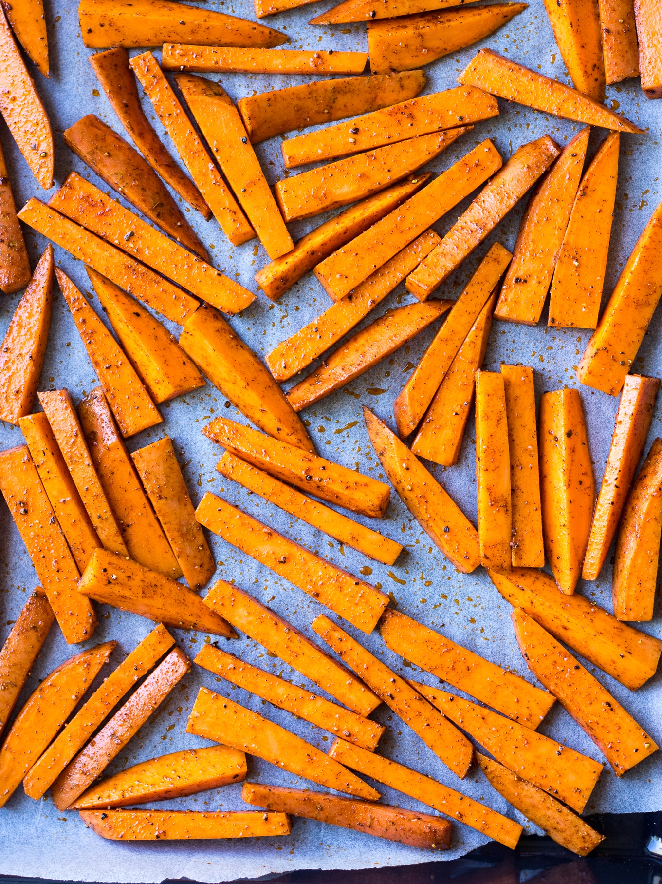 Cinnamon Paprika Sweet Potato Fries spread on lined baking tray before baking.