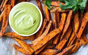 Cinnamon Paprika Sweet Potato Fries arranged on a plate with dipping sauce and herbs.