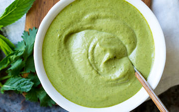 Cashew Tahini Herb Sauce in a white serving bowl with spoon and fresh herbs.