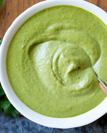 Cashew Tahini Herb Sauce in a white serving bowl with spoon and fresh herbs.