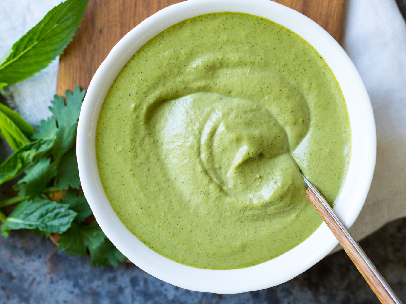 Cashew Tahini Herb Sauce in a white serving bowl with spoon and fresh herbs.