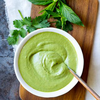 Cashew Tahini Herb Sauce in a white bowl with a spoon, on a chopping board.