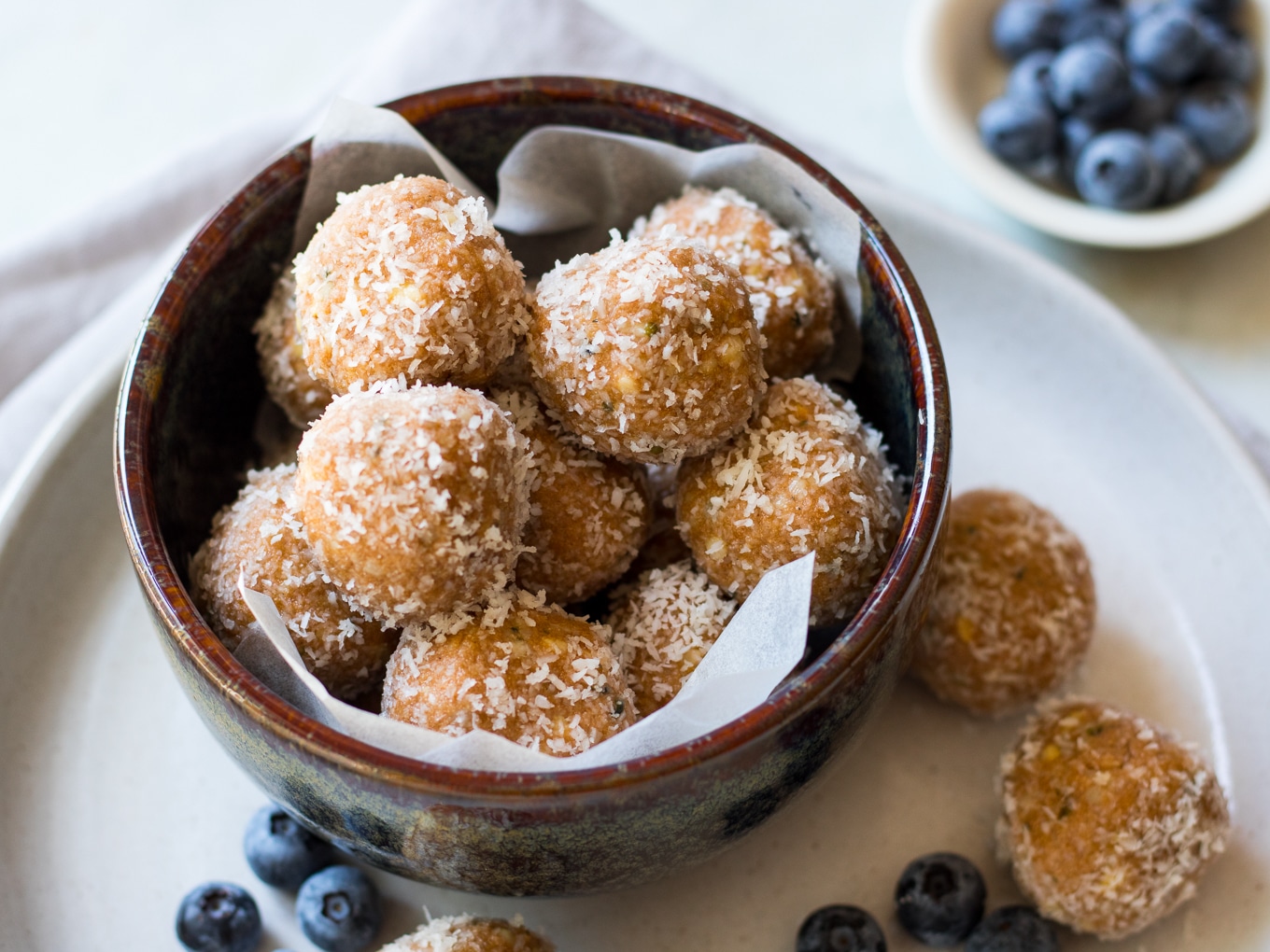 No food processor Paleo Protein Balls stacked in a bowl. Recipe made with crunchy nut butter, coconut, hemp seeds, honey and protein powder. 