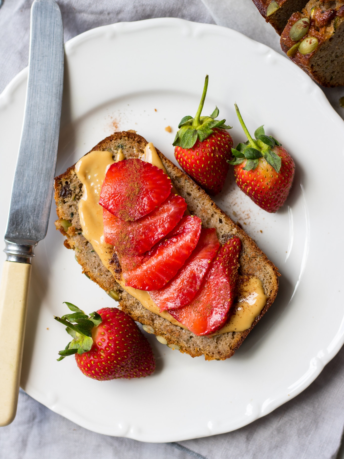 Slice of apple zucchini snack cake on a white side plate with knife, sliced strawberries on top
