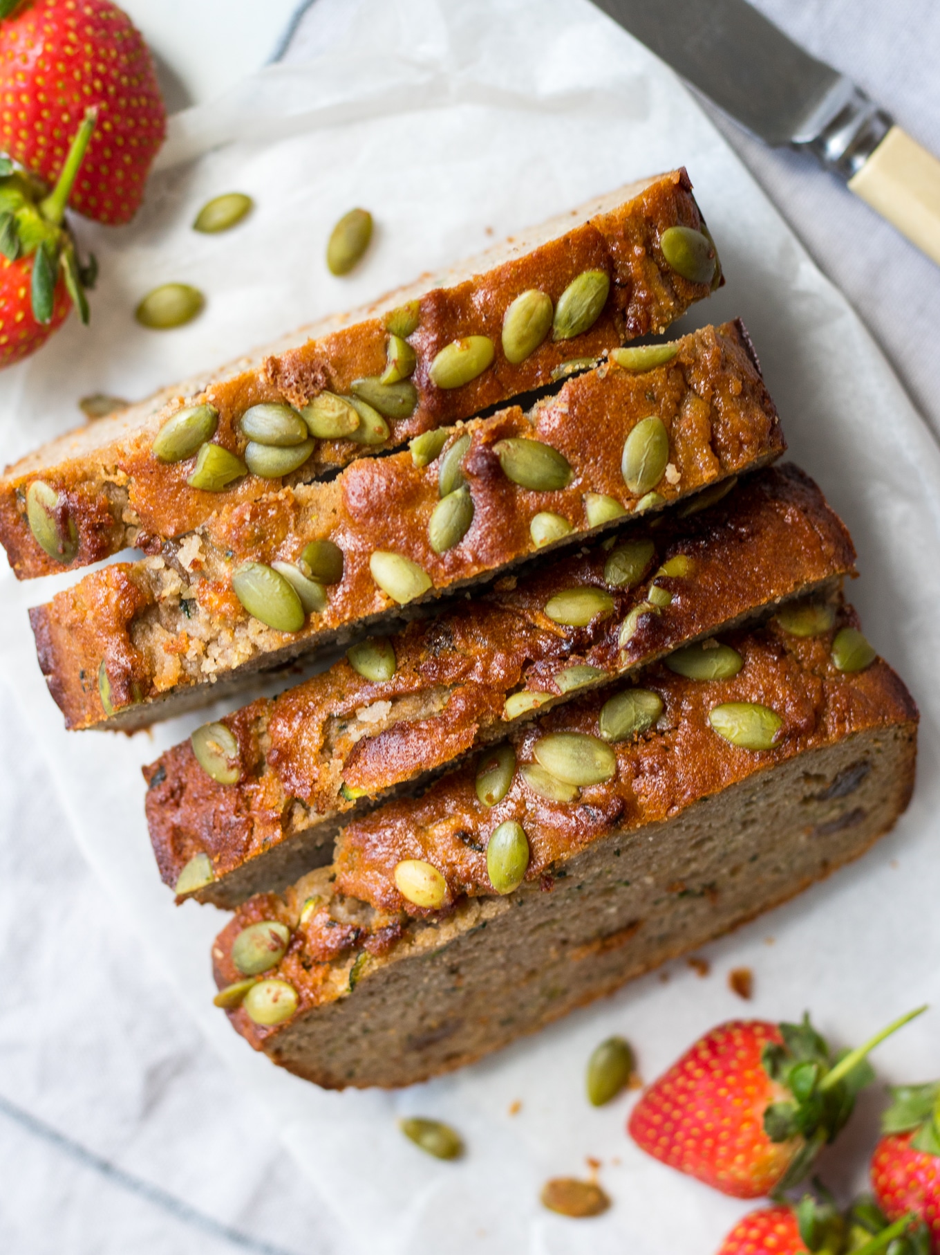 Four slices of apple zucchini snack cake on white background, shot from above, strawberries scattered around