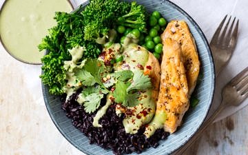 Chicken black rice bowl, one blue serving bowl filled with rice, marinated chicken, broccolini, peas and creamy herb sauce