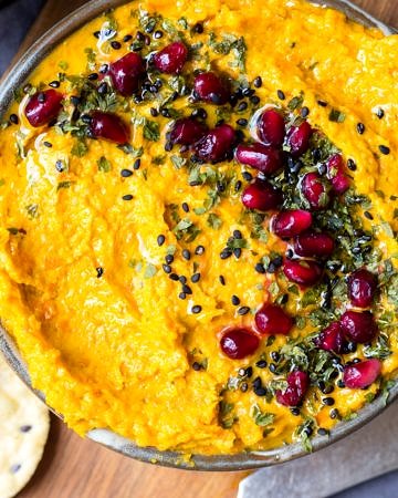 Roasted carrot tahini tip in a small grey dish on a wooden chopping board.