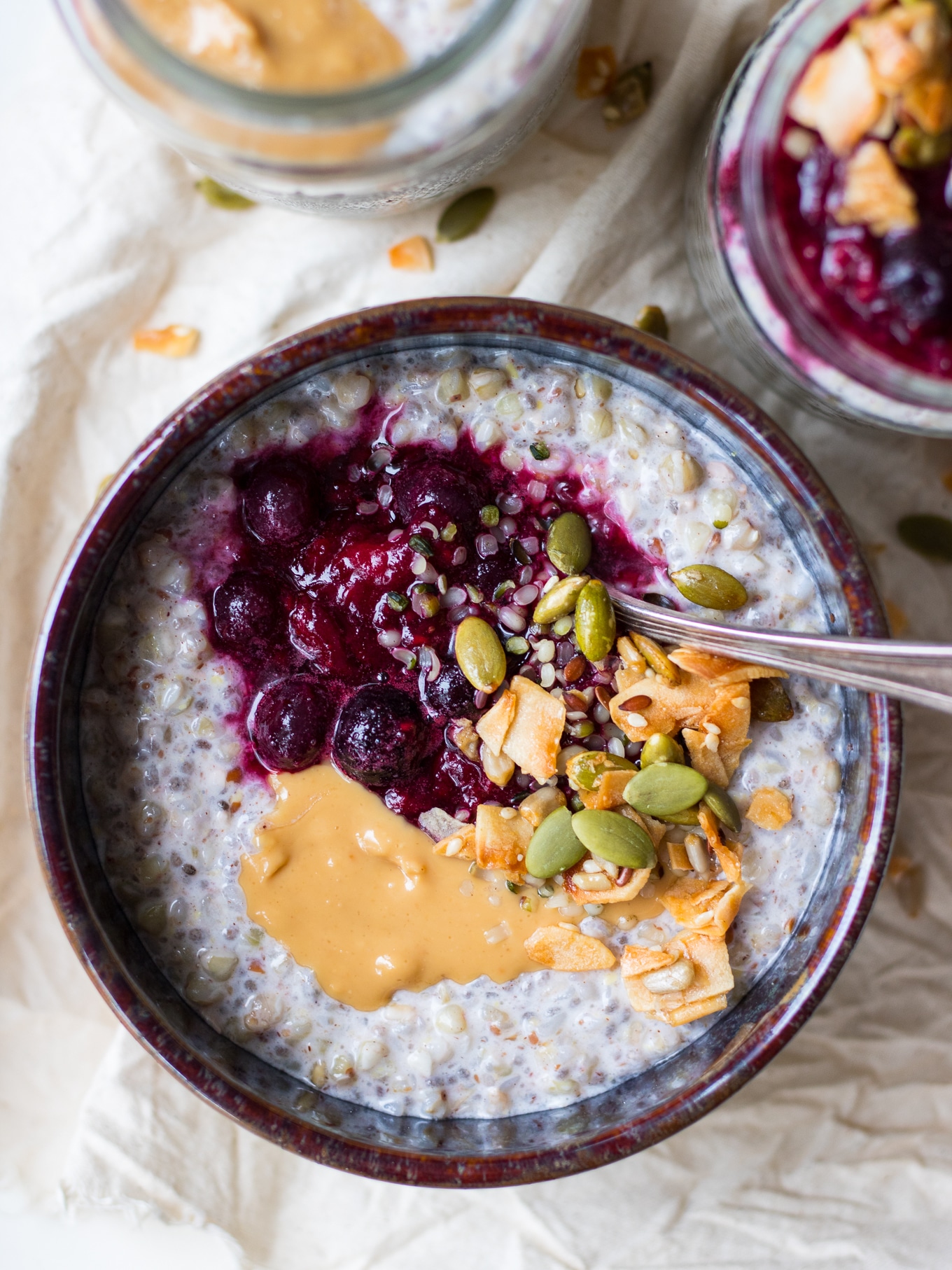 Close up of buckwheat bircher in blue bowl, nut butter and berries on top, top down view