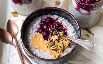 Buckwheat bircher in a small blue ceramic bowl, berries, nut butter and granola on top