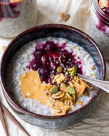 Buckwheat bircher in a small blue ceramic bowl, berries, nut butter and granola on top