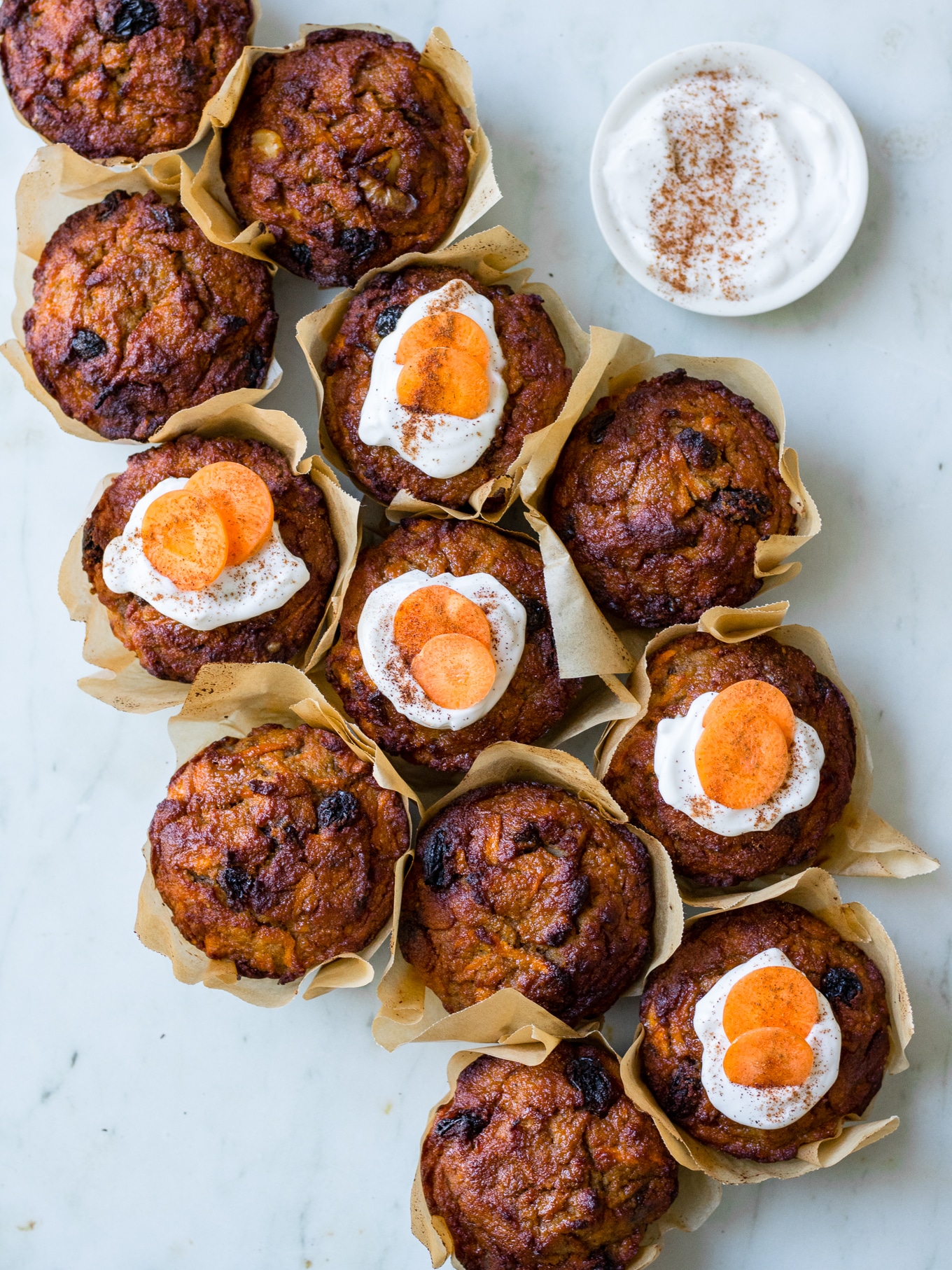 Healthy Carrot Cake Muffins, muffins clustered together on a marble surface, half iced with coconut yoghurt