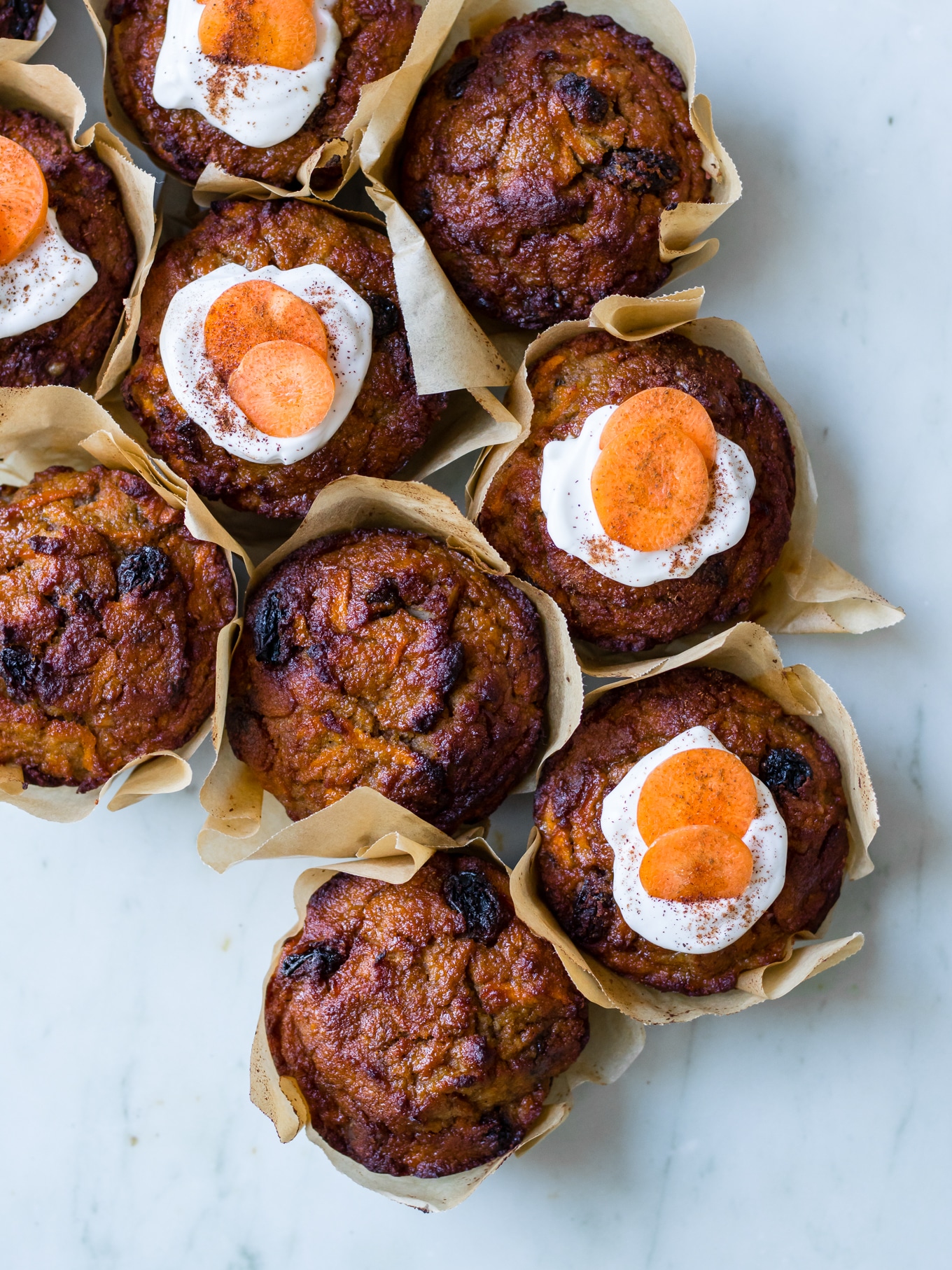 Healthy Carrot Cake Muffins, muffins clustered together on a marble surface, half iced with coconut yoghurt