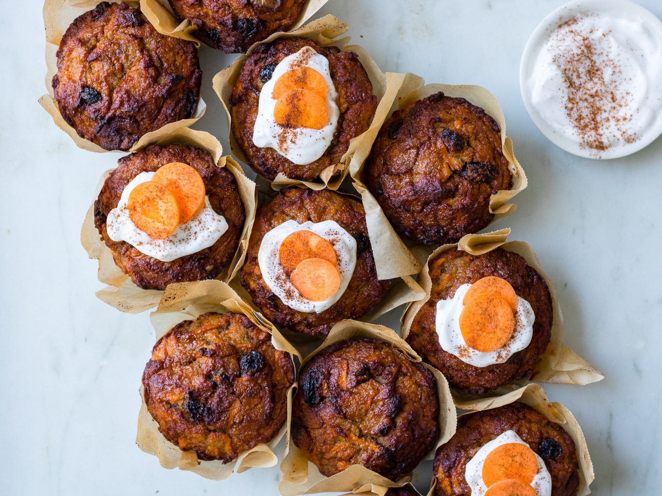 Healthy Carrot Cake Muffins, muffins clustered together on a marble surface, half iced with coconut yoghurt