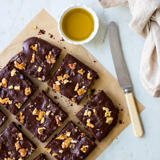 Olive oil chocolate brownies on brown baking paper, on an angle, with butter knife, and olive oil in small dish