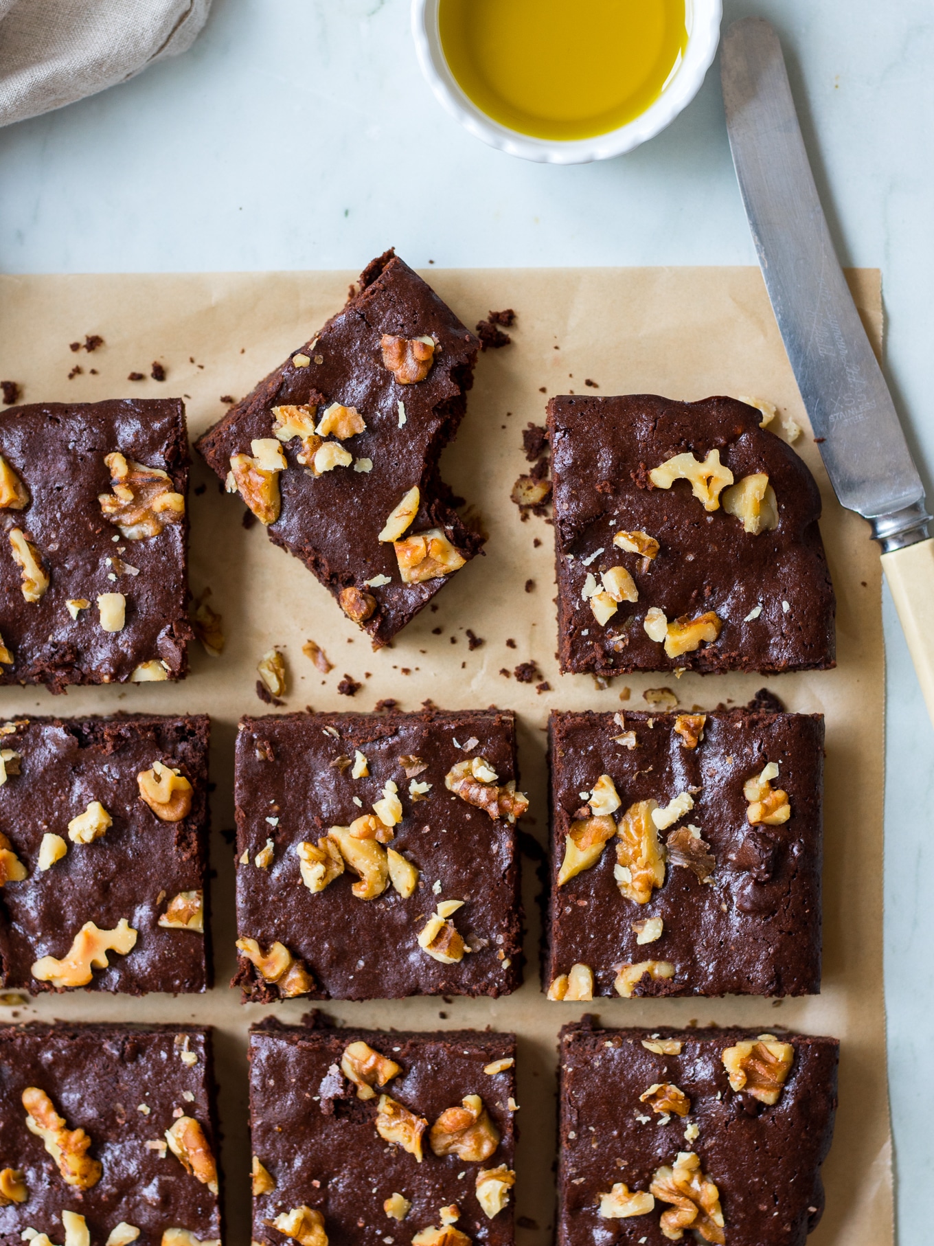 Olive oil chocolate brownies on brown baking paper, one bitten and on an angle, butter knife on side