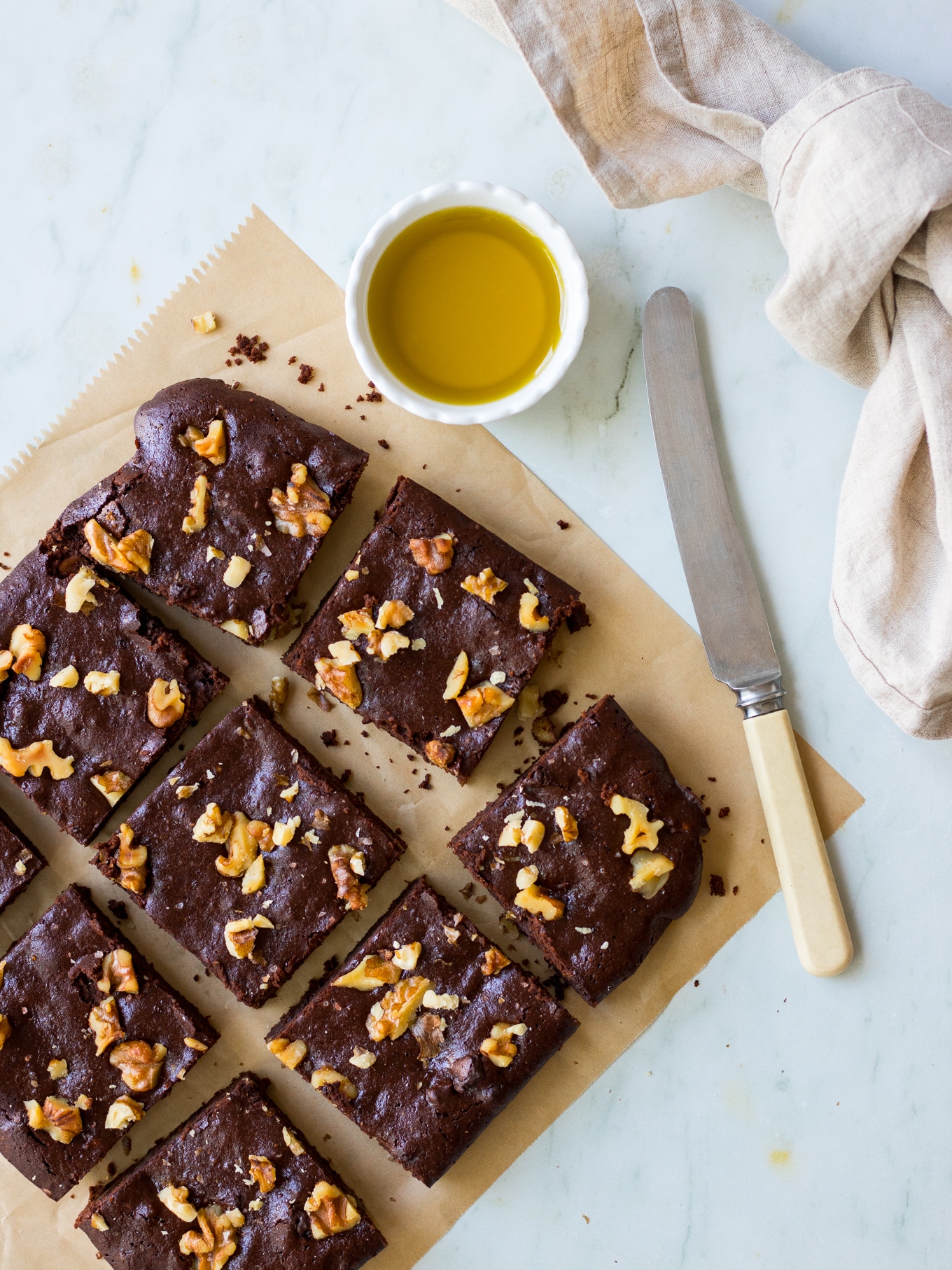 Olive oil chocolate brownies on brown baking paper, on an angle, with butter knife, and olive oil in small dish
