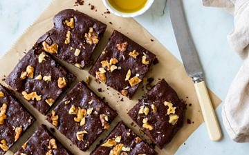 Olive oil chocolate brownies on brown baking paper, on an angle, with butter knife, and olive oil in small dish