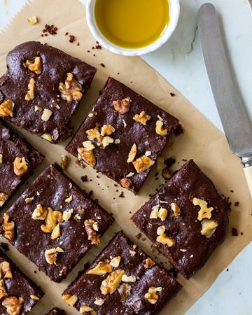 Olive oil chocolate brownies on brown baking paper, on an angle, with butter knife, and olive oil in small dish