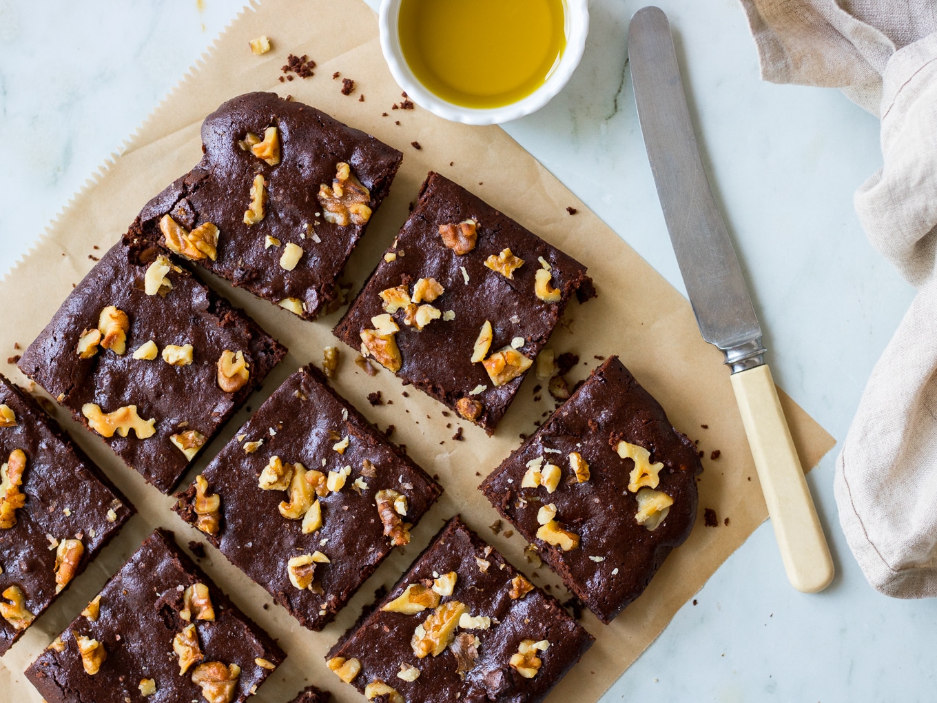 Olive oil chocolate brownies on brown baking paper, on an angle, with butter knife, and olive oil in small dish