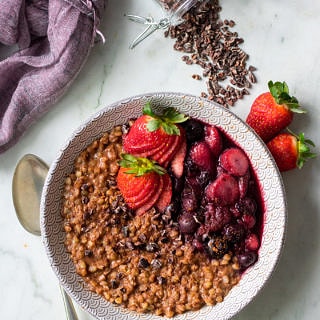 Top view of chocolate buckwheat porridge with stewed berries, cacao nibs scattered around