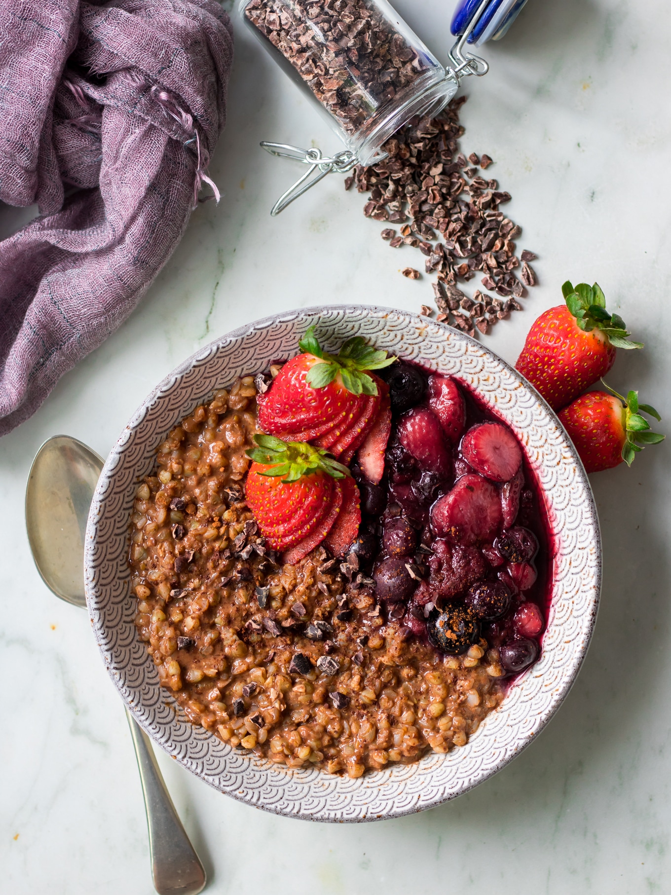 Top view of chocolate buckwheat porridge with stewed berries, cacao nibs scattered around