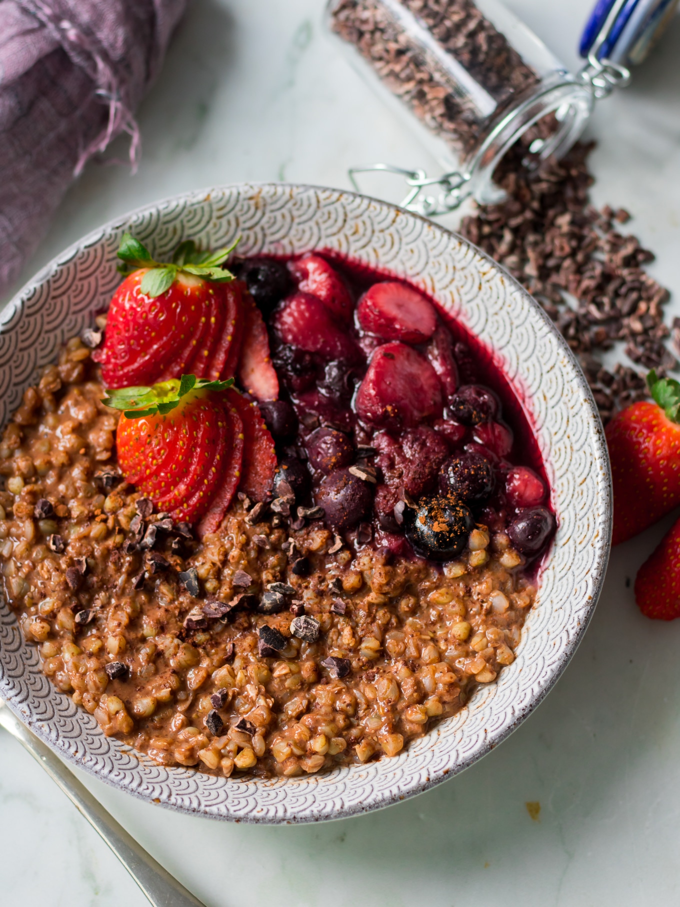 Angle view of chocolate buckwheat porridge in patterned bowl, scattered cacao nibs, berries on top