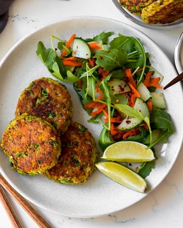 thai salmon cakes on white plate with side salad and lime