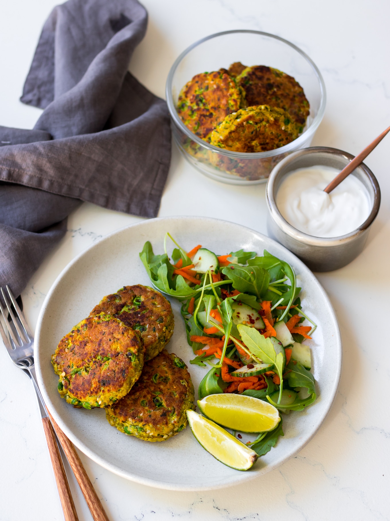thai salmon cakes on white plate with side salad, yoghurt and lime