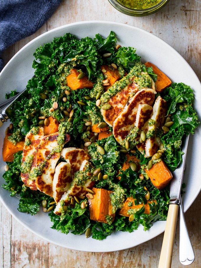 Halloumi kale salad in grey ceramic bowl, pesto sauce, wooden table top