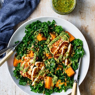 Halloumi kale salad in grey ceramic bowl, pesto sauce, wooden table top