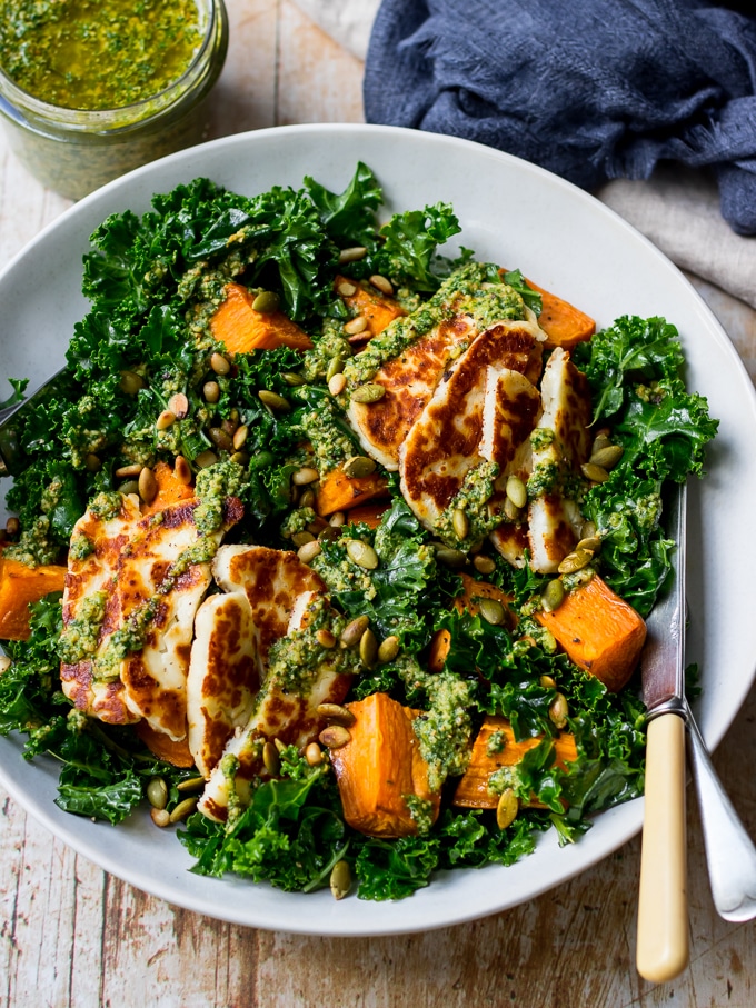 Halloumi kale salad in grey ceramic bowl, pesto sauce, wooden table top