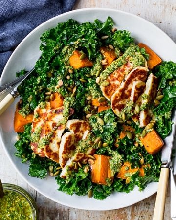 Halloumi kale salad in grey ceramic bowl, pesto sauce, wooden table top