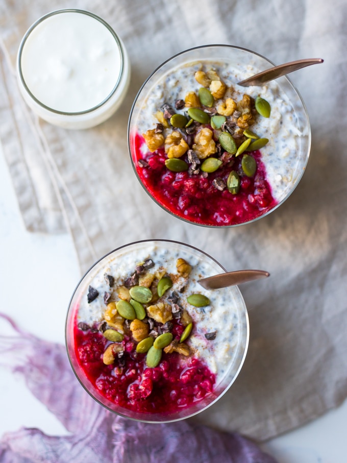 raspberry kefir overnight oats glasses top down view, topped with nuts, seeds, cacao