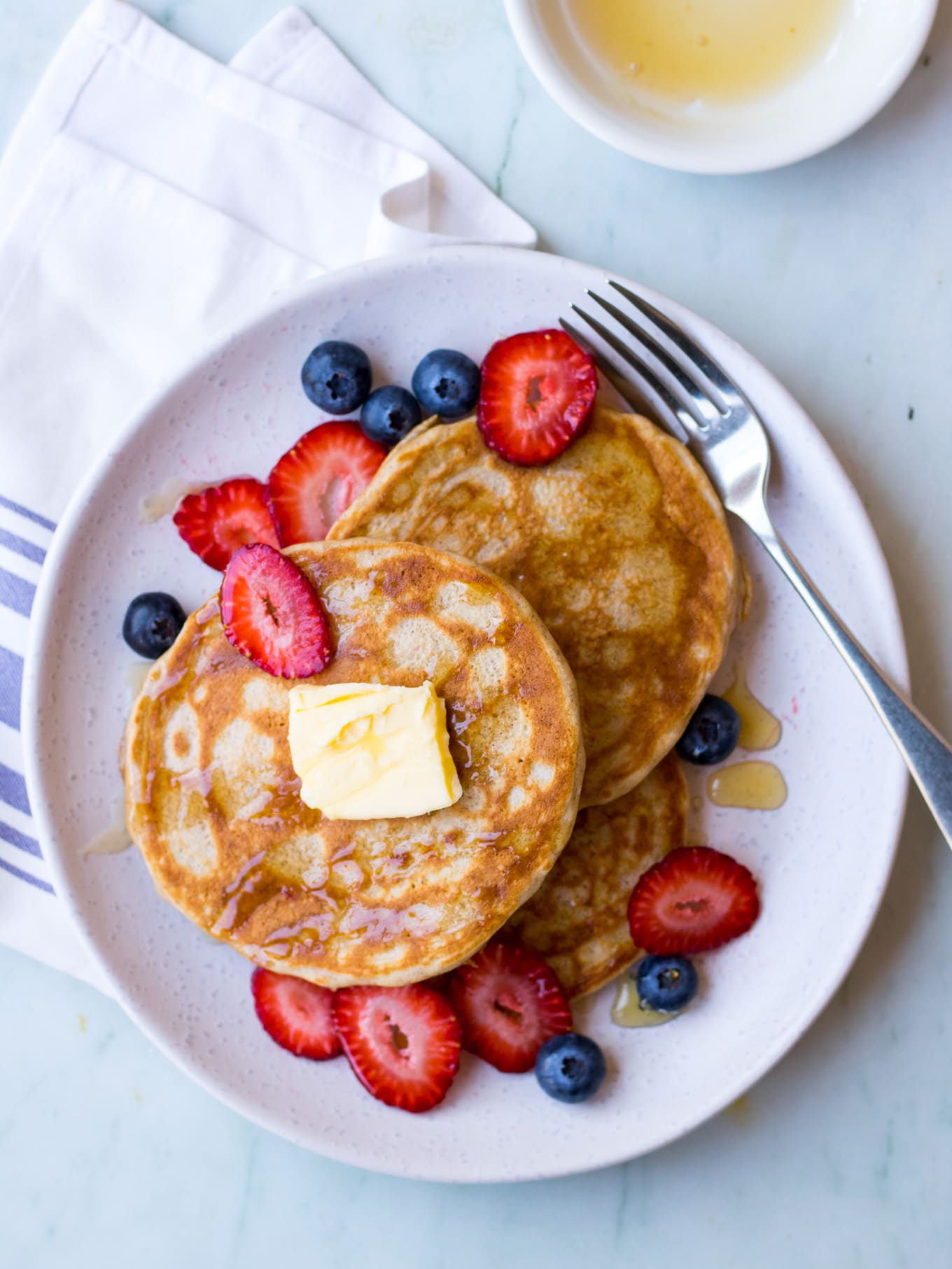 gluten free buckwheat pancakes on a white ceramic plate with fresh berries and maple syrup