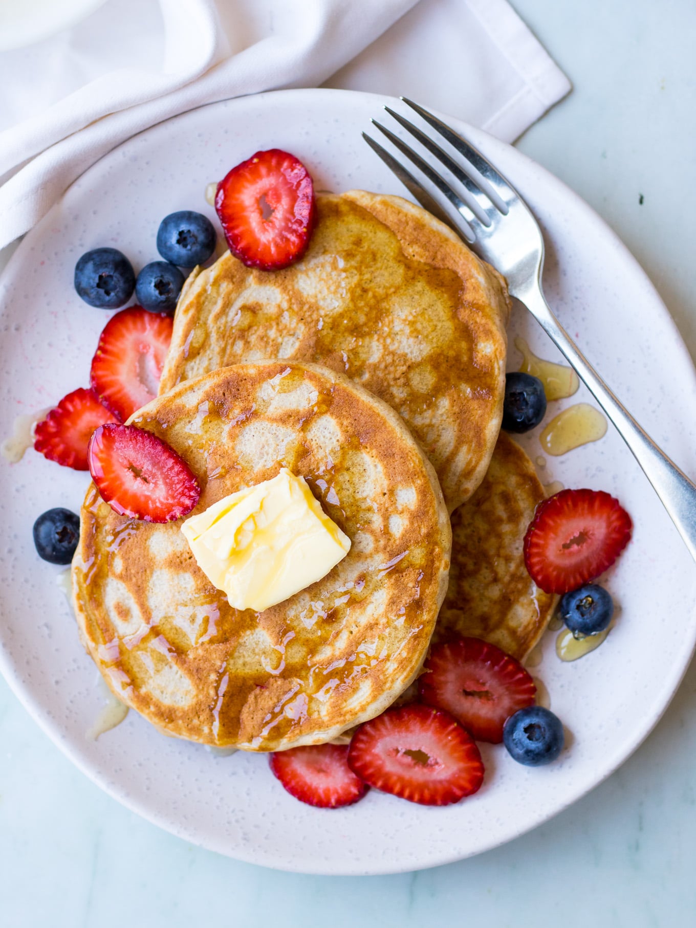 gluten free buckwheat pancakes on a white ceramic plate with fresh berries and maple syrup