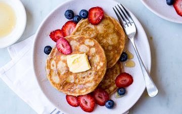 gluten free buckwheat pancakes on a white ceramic plate with fresh berries and maple syrup