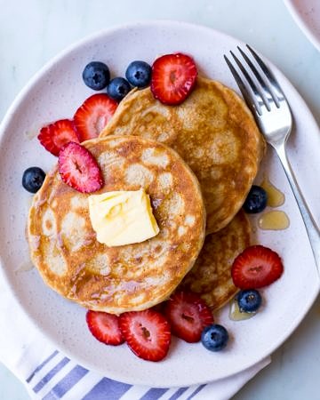 gluten free buckwheat pancakes on a white ceramic plate with fresh berries and maple syrup