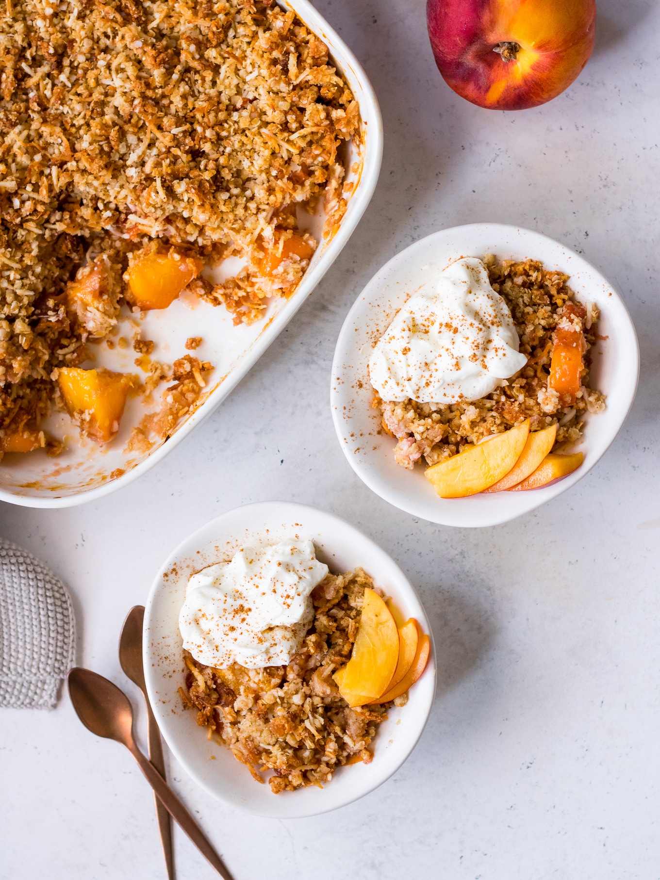 Small bowls of gluten free stone fruit crumble topped with nectarine slices and yoghurt