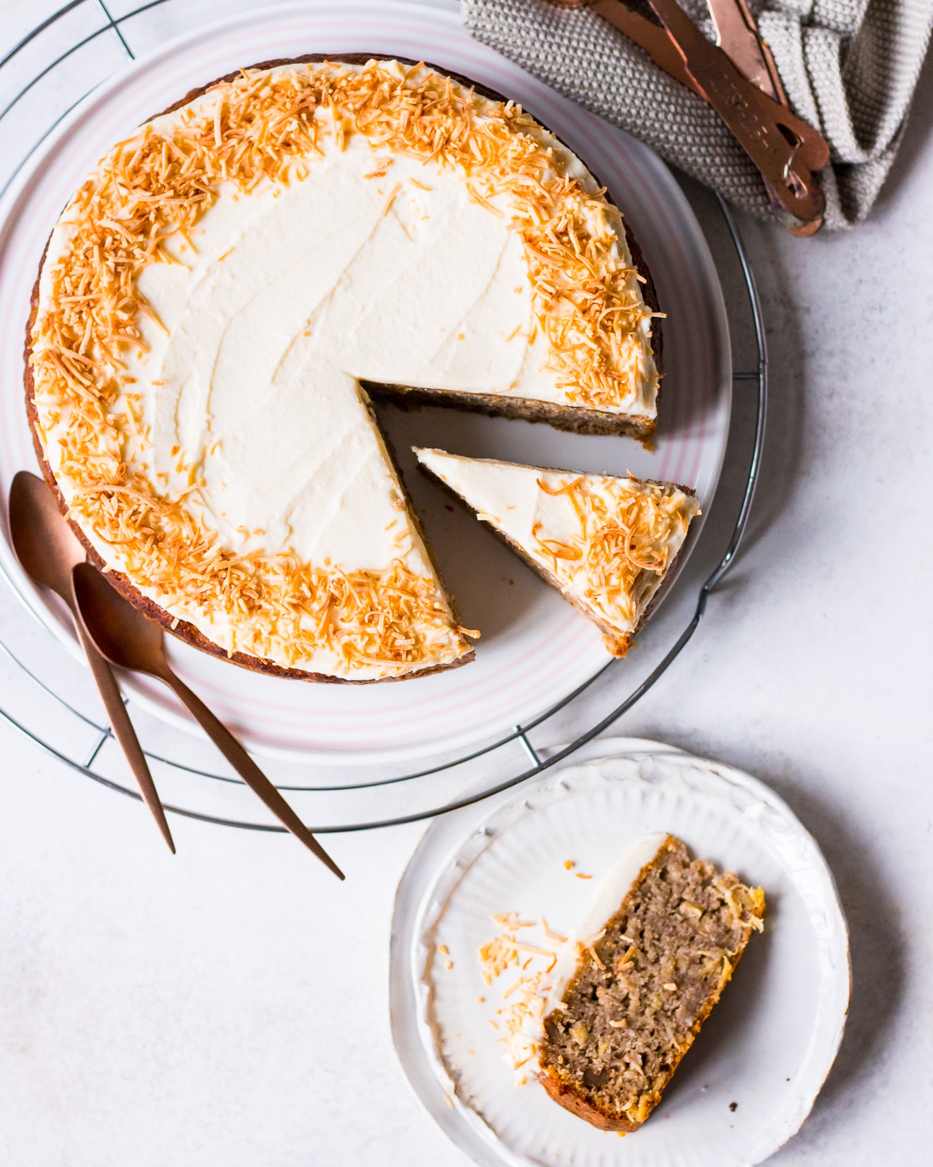 Flatlay of hummingbird cake with slice on plate, shredded coconut on frosting