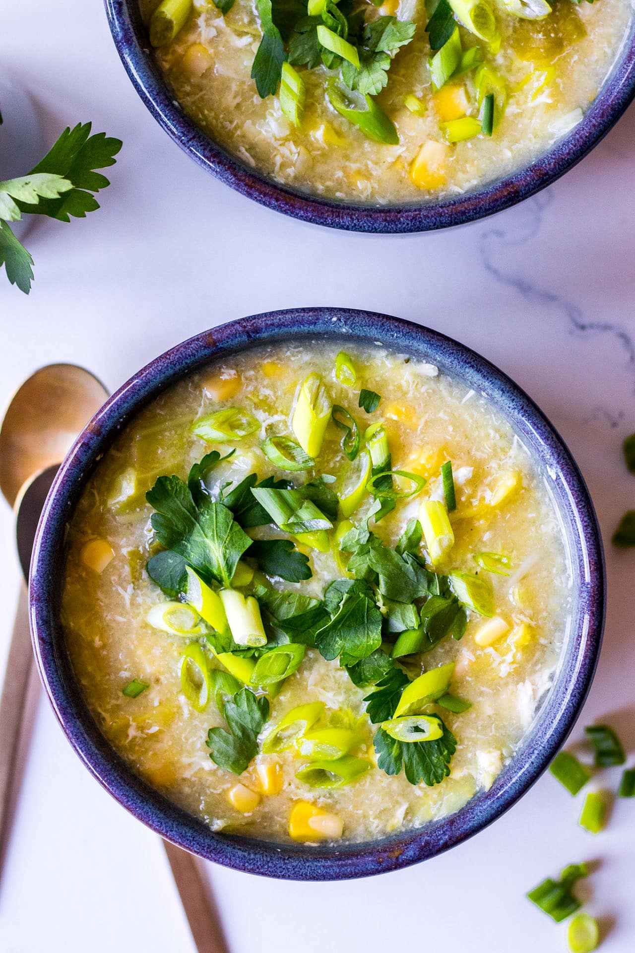 Blue ceramic bowl filled with chicken sweet corn soup and topped with spring onion