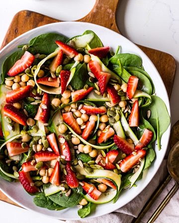 Strawberry, chickpea and spinach salad in a wide bowl on wooden chopping board