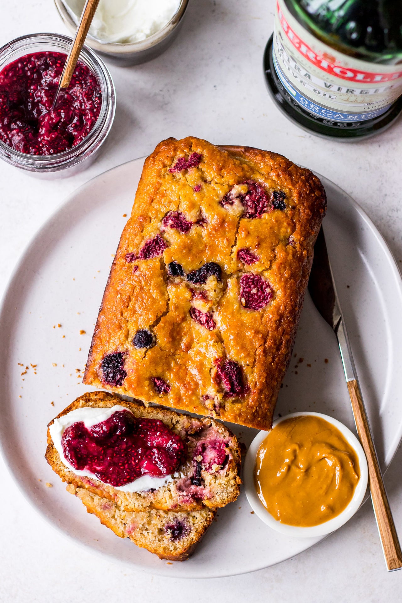 Top view of a berry loaf cake on white ceramic plate with peanut butter and jam
