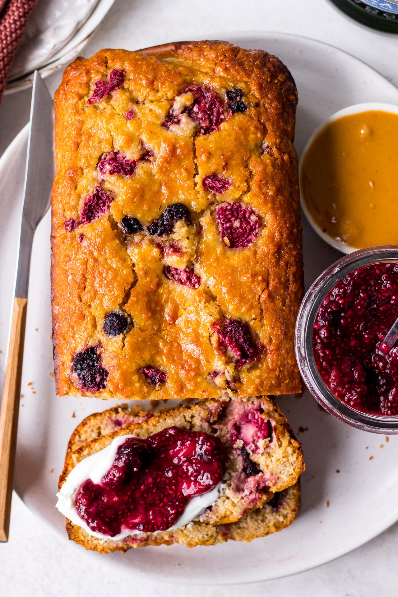top view of mixed berry yoghurt loaf on white plate with yoghurt and chia jam