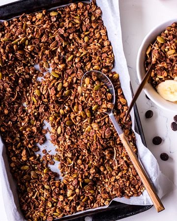Tray of chocolate olive oil granola with a spoon, small bowl to the side