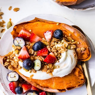 Baked sweet potato on white plate topped with Greek yoghurt, berries and granola