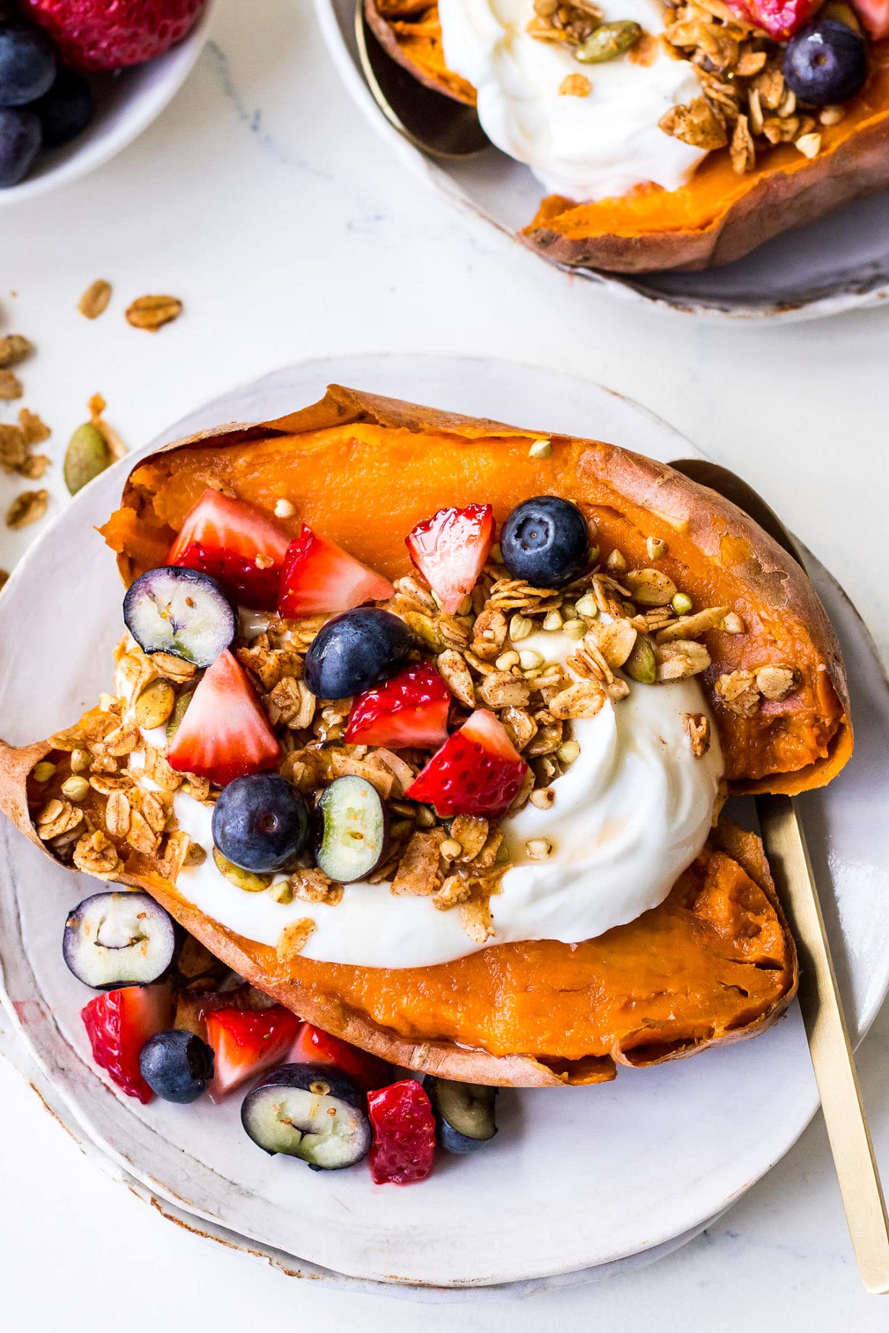 Baked sweet potato on white plate topped with Greek yoghurt, berries and granola