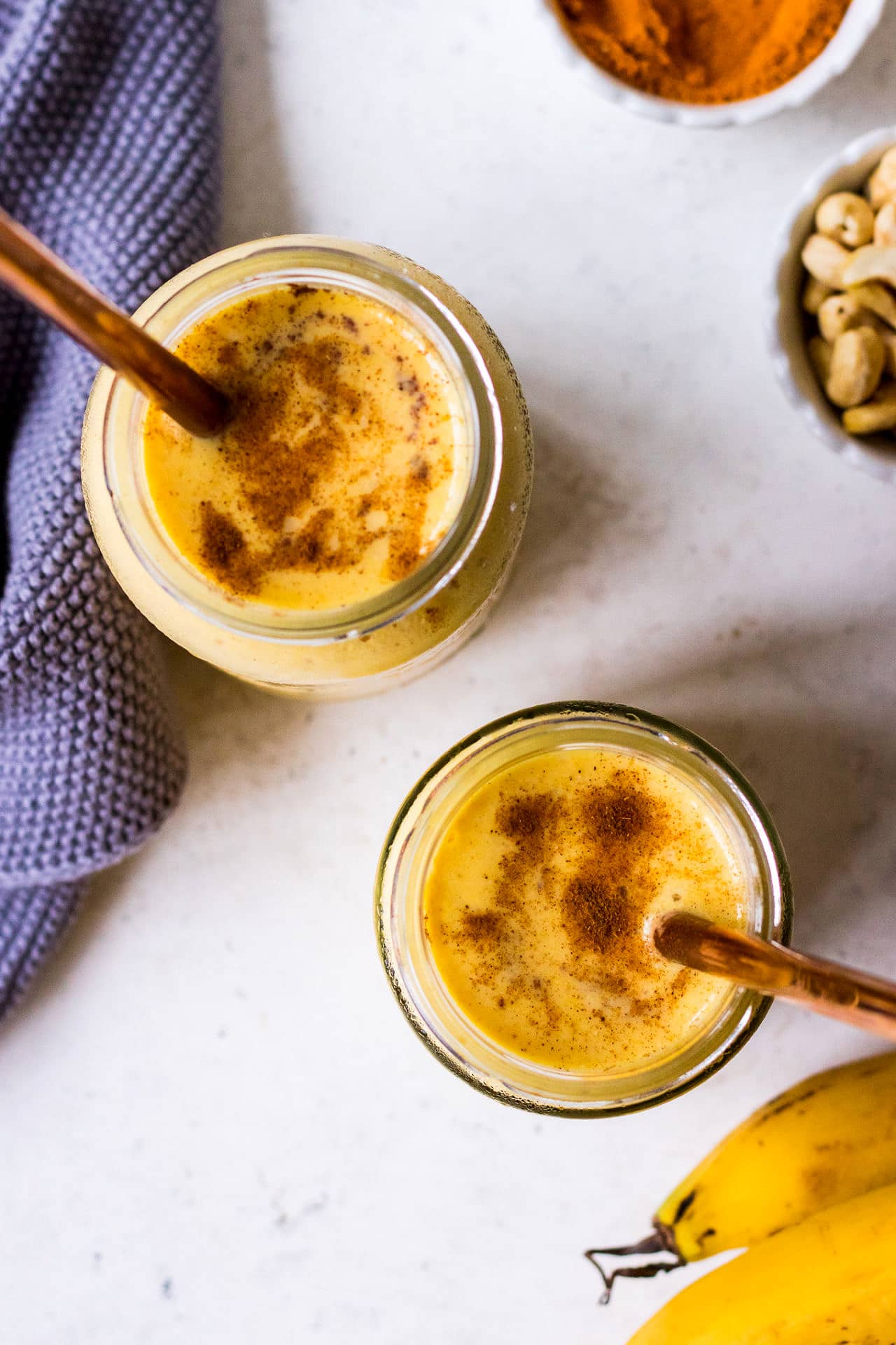 Top down view of golden milk smoothie in glass jars with copper straws and blue napkin